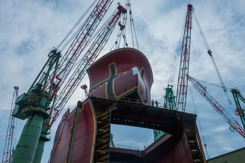 Shipyard cranes lifting a hull section over a building dock.