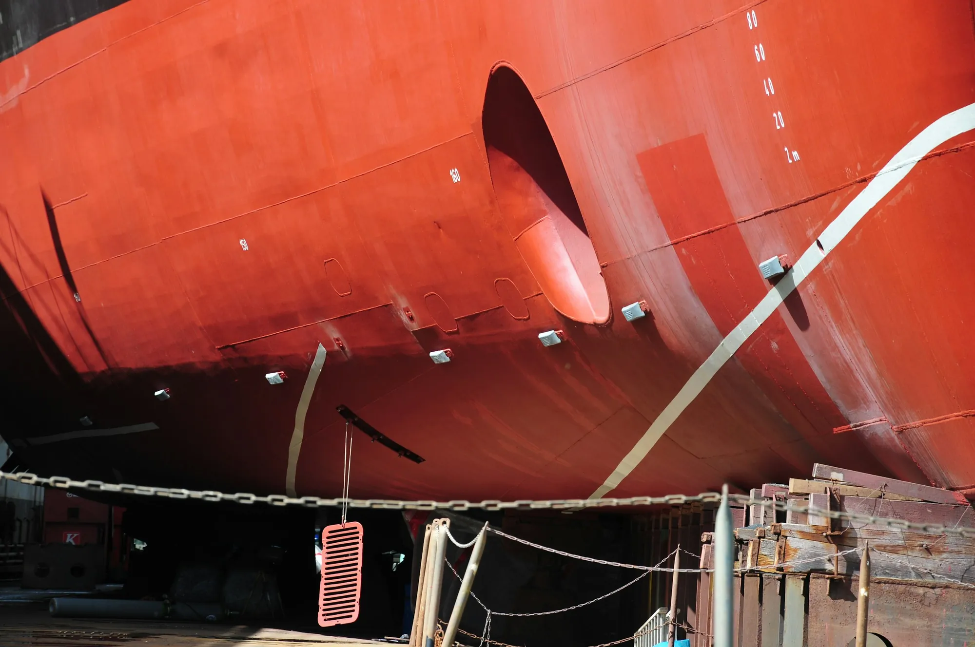A ship's red hull and propeller seen from below in a dry dock.
