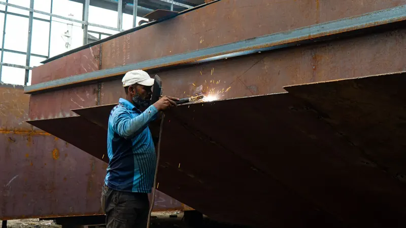 A welder working on a large steel structure, sparks falling.