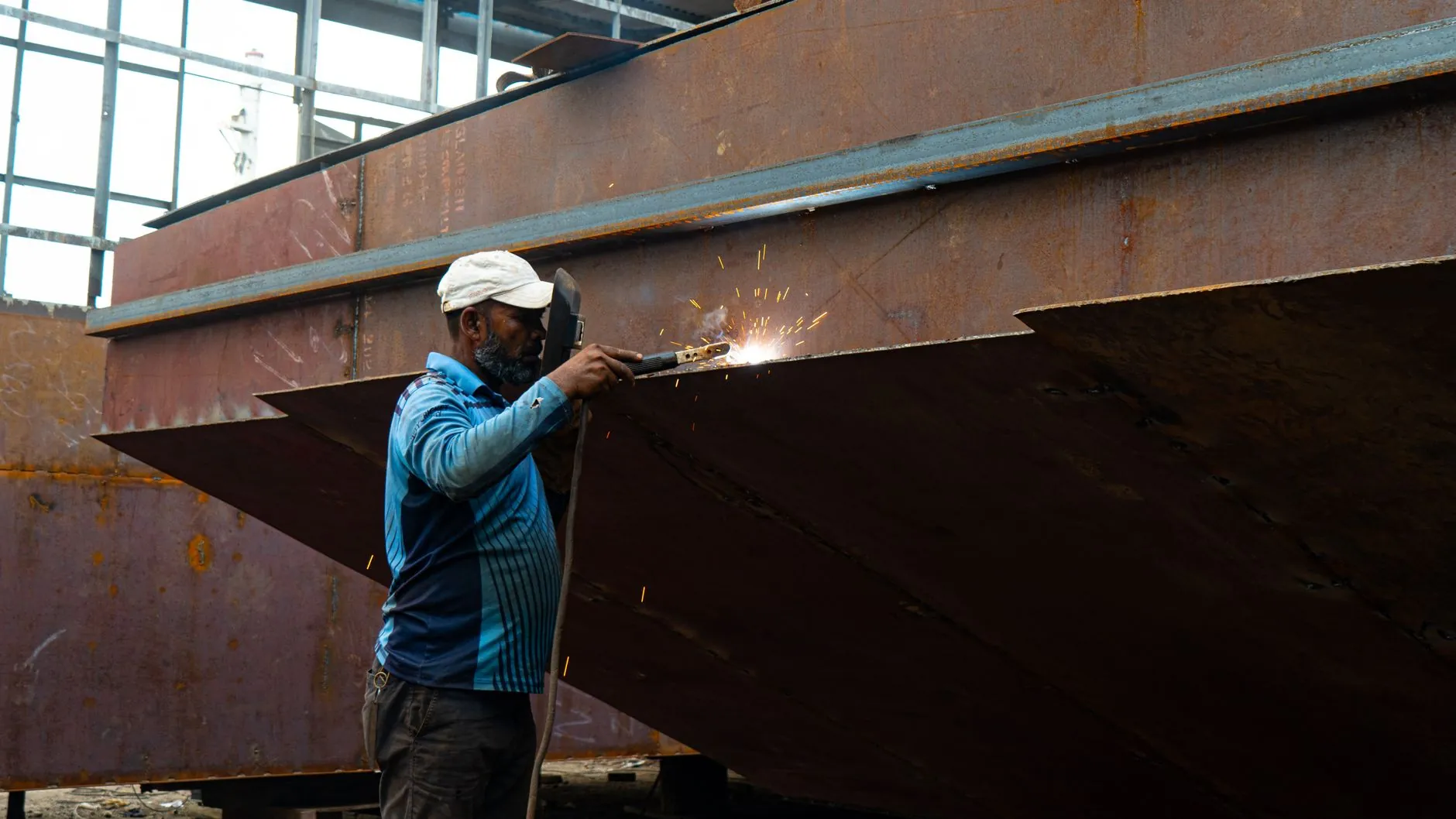 A welder working on a large steel structure, sparks falling.