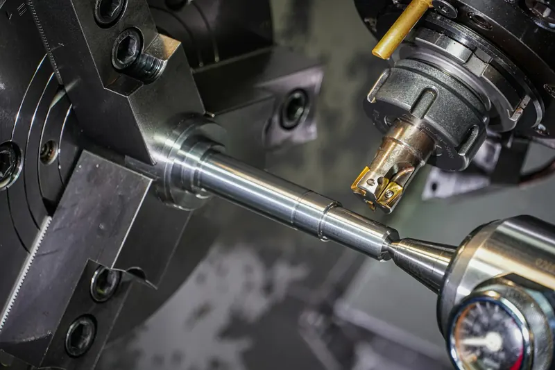 A shaft held in a three-jaw chuck on a lathe, ready for cutting.