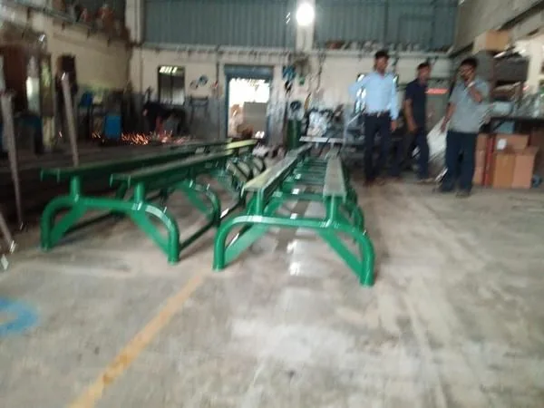 A row of green painted handling cradles lined up in a workshop with staff standing behind them.