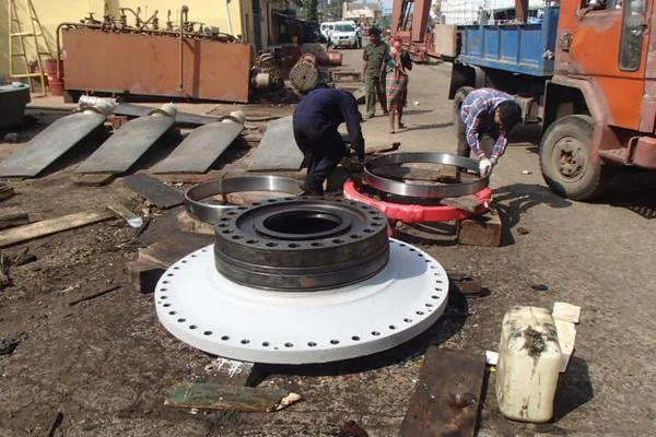A large machined flange ring laid out on the yard with fitters working on it beside a lorry.