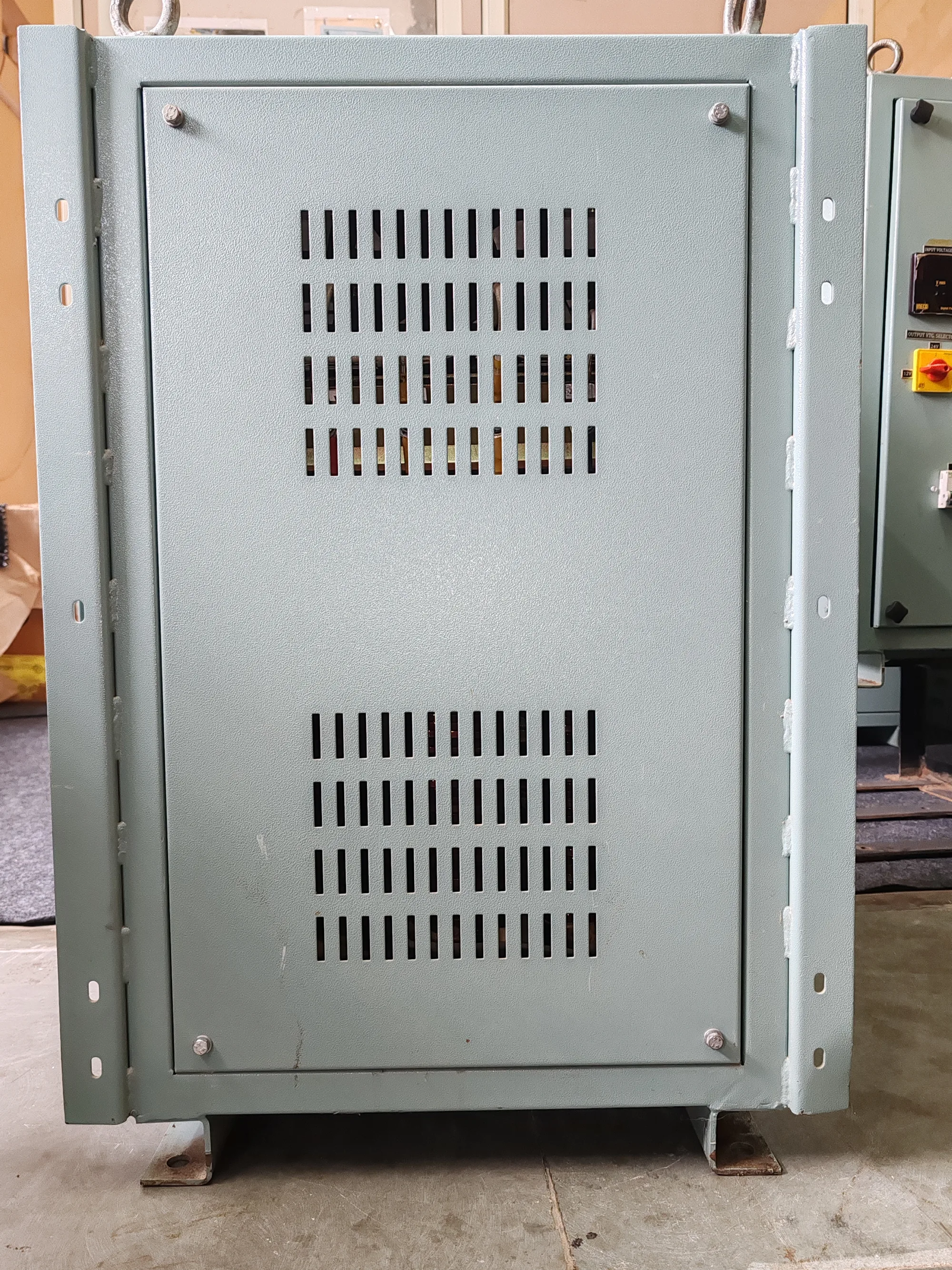 The louvred side of a rectifier cabinet, lifting eyes at the top and a bolted mounting base.