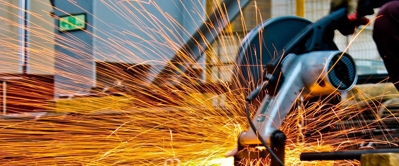 An angle grinder throwing sparks across a steel component on the workshop floor.